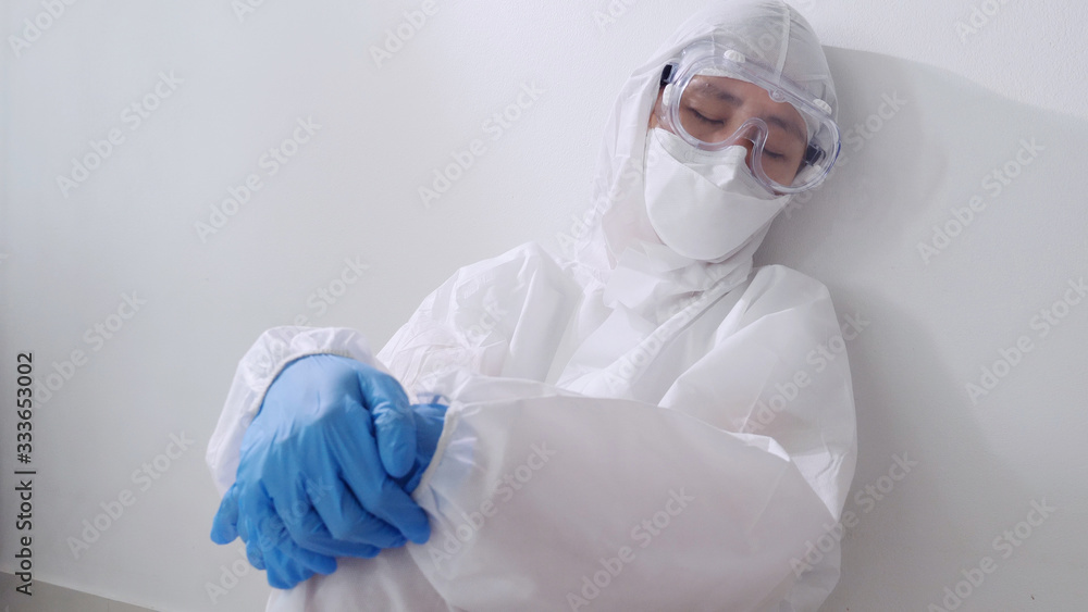 Tired Asian doctor in PPE suit sitting and sleeping on the floor, Overworked doctor
