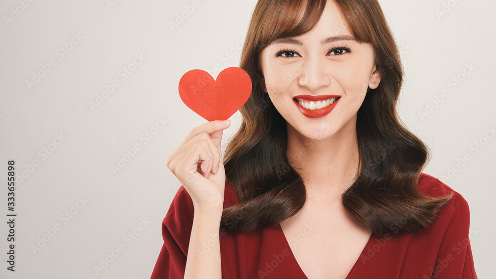 Pretty young Asian woman holding white paper heart and smiling happily at camera