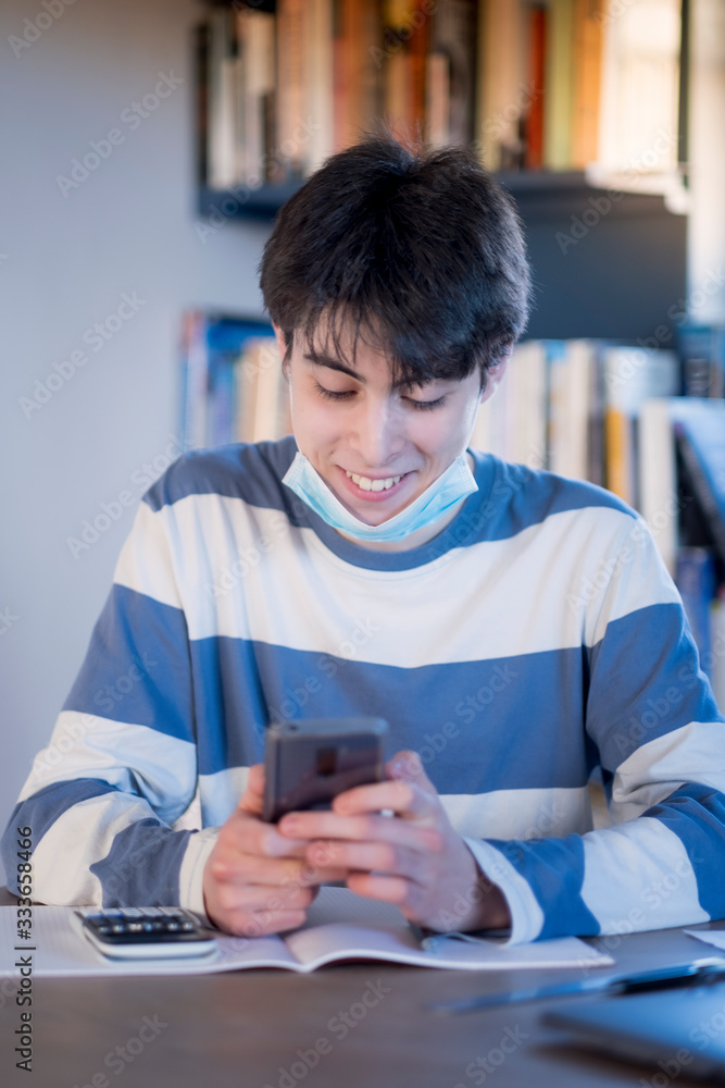 A teenager at home using a protective face mask and texting on his mobile phone A teenager at home using a protective face mask and texting on his mobile phone