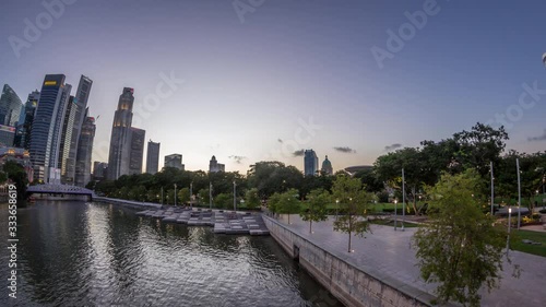 Singapore skyscrapers skyline with white Anderson Bridge and a few towers of financial district near esplanade park park day to night transition timelapse. Some green foliage on both sides. photo