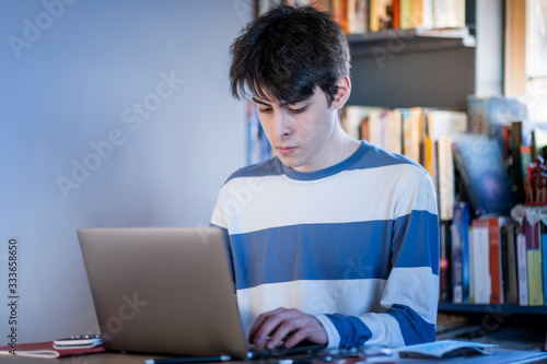 A teenaged boy studying on his computer at home in his living room