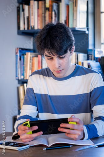 A teenager taking a break from homework to play on his game console