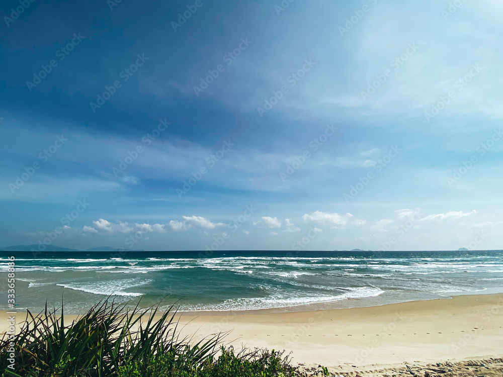 Sandy seashore, calm soft waves at sea, sunny weather, blue sky with white clouds