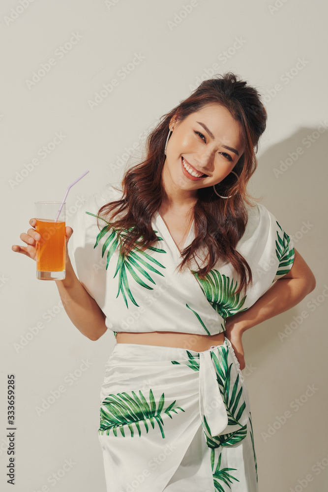 Beautiful young Asian woman with orange juice in tropical shirt on white background Beautiful young Asian woman with orange juice in tropical shirt on white background