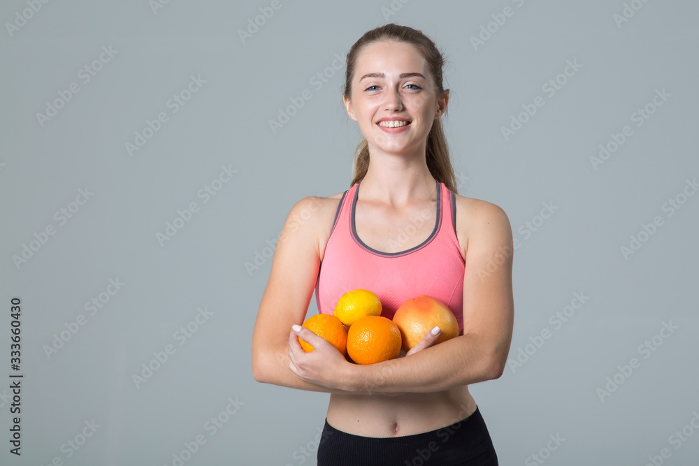 Young woman holds citrus fruits, lemon and orange in her hands, standing on a gray background and looking at the camera. Young woman holds citrus fruits, lemon and orange in her hands, standing on a gray background and looking at the camera.