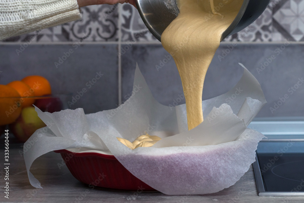 The hostess prepares apple charlotte at home in the kitchen and pours the dough into a baking dish The hostess prepares apple charlotte at home in the kitchen and pours the dough into a baking dish