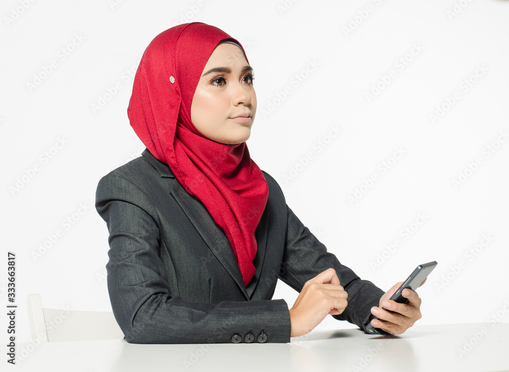 Communication concept, young woman with hijab sitting and texting her friends using her handphone against white background Communication concept, young woman with hijab sitting and texting her friends using her handphone against white background