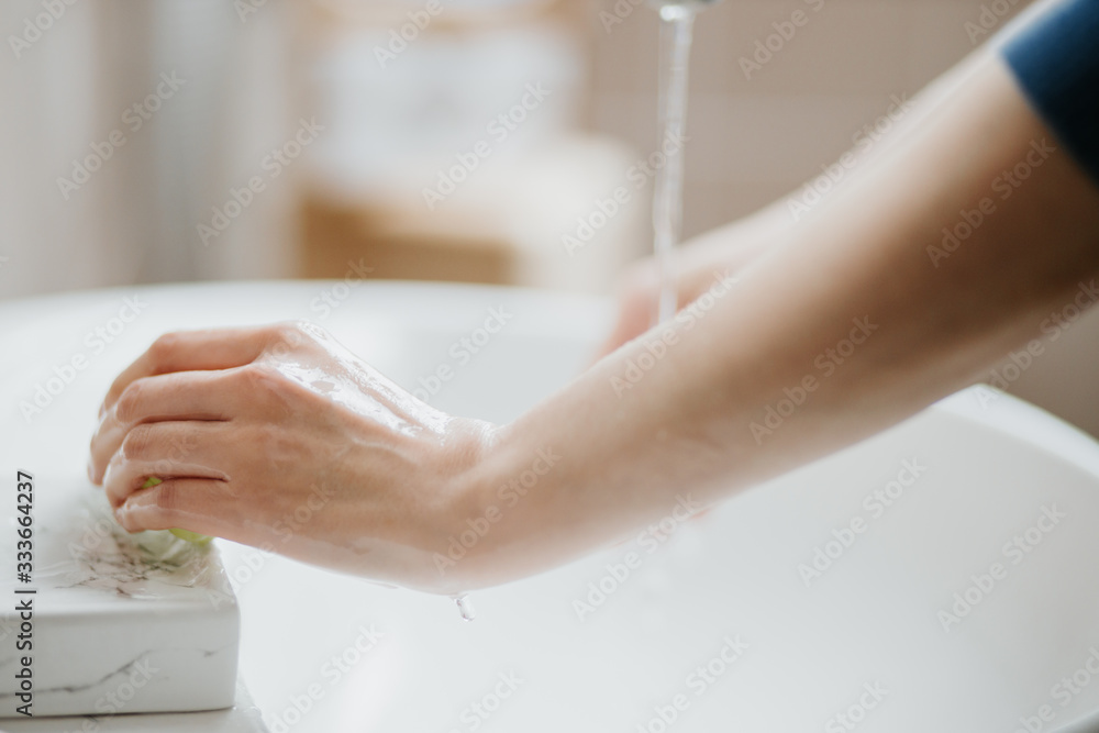Obraz premium Closeup of a woman washing her hands in bathroom to prevent Covid-19 viral infection. Recommended washing with soap and running water during coronavirus pandemic.