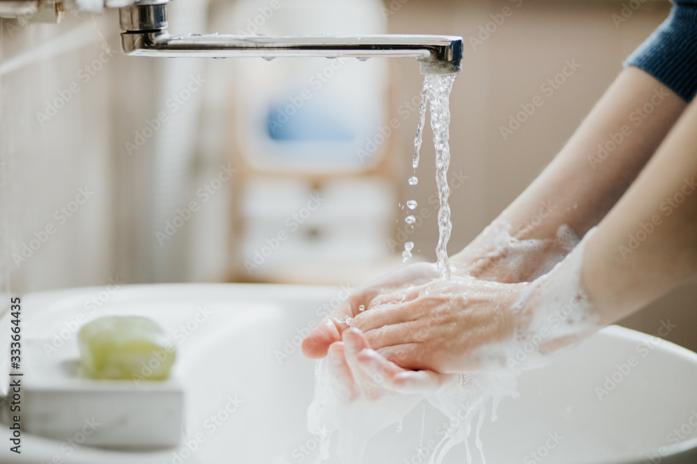 Closeup of a woman washing her hands in bathroom to prevent Covid-19 viral infection. Recommended washing with soap and running water during coronavirus pandemic. - obrazy, fototapety, plakaty 