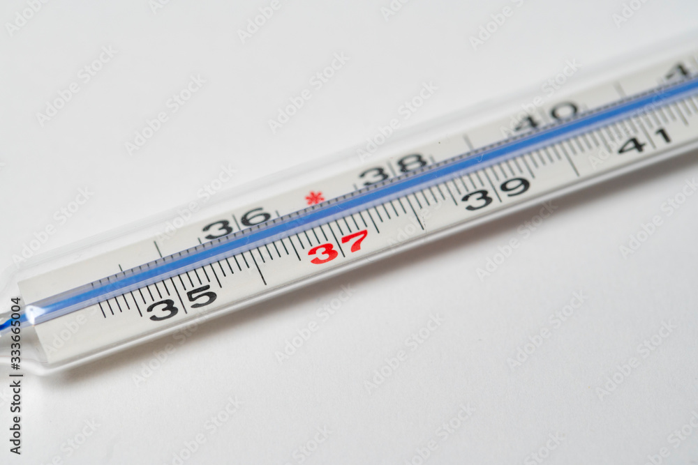 Mercury in glass thermometer on white surface. Copy space on top and bottom. Fever thermometer in analog form for measuring high temperature due to illness like flu or coronavirus Mercury in glass thermometer on white surface. Copy space on top and bottom. Fever thermometer in analog form for measuring high temperature due to illness like flu or coronavirus