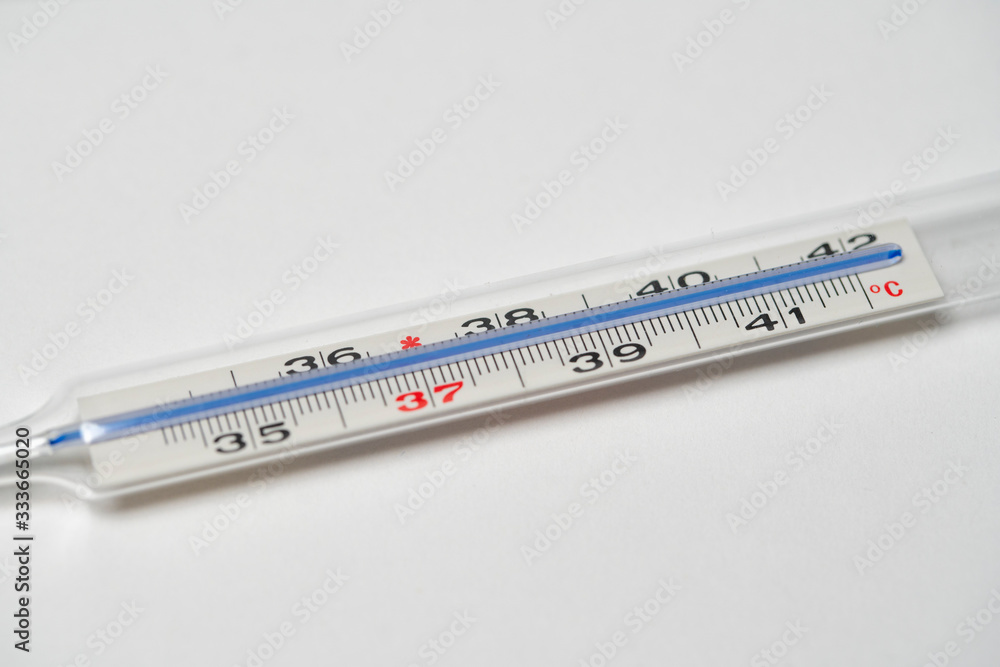 Mercury in glass thermometer on white surface. Copy space on top and bottom. Fever thermometer in analog form for measuring high temperature due to illness like flu or coronavirus Mercury in glass thermometer on white surface. Copy space on top and bottom. Fever thermometer in analog form for measuring high temperature due to illness like flu or coronavirus