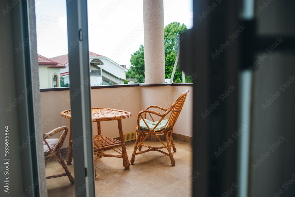 Room that opens with doors onto a terrace with wicker table and chairs.