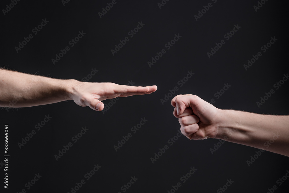 Men's hands on a dark background, show a game of stone, scissors, paper. The concept of confrontation and rivalry, games