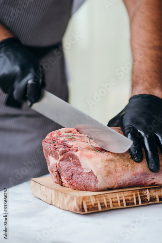 Chef cutting raw beef on chopping board, professional cook in gloves holding knife and cutting meat for steak.