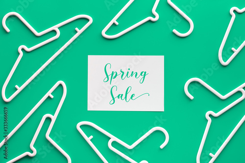 White plastic hangers, text "Spring sale" on paper. Creative top view flat lay on trendy pastel green mint background, geometric composition, creative minimalism. Flat lay, Springtime sale online.
