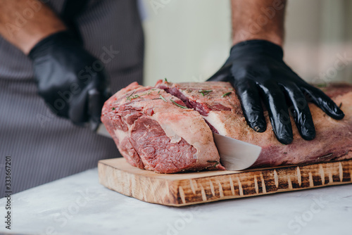 Chef cutting raw beef on chopping board, professional cook in gloves holding knife and cutting meat for steak.