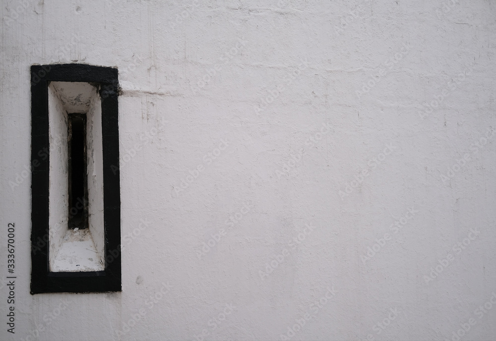 One old antique window with a black frame with flaky paint on a white stone wall. One old antique window with a black frame with flaky paint on a white stone wall.