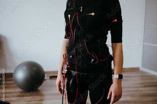 Woman in EMS electro stimulation suit with cables.