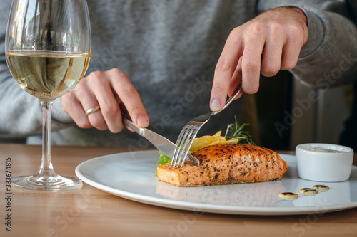 Horizontal close-up of man eating salmon fish steak. Crispy grilled salmon steak with lemon, salad and rosemary, white wine and white sauce. © ChesterAlive91