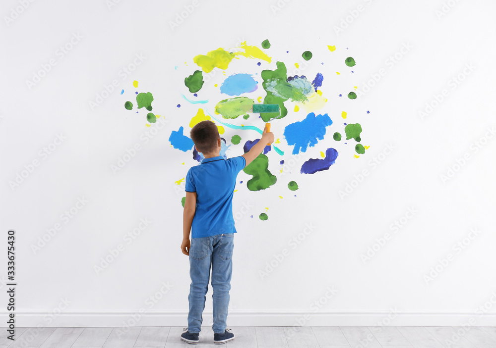 Little boy drawing on white wall indoors, back view Little boy drawing on white wall indoors, back view