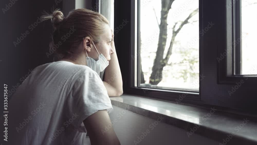 4k side view closeup of worried young Caucasian woman with blonde hair and white shirt wearing medical protection face mask watching the city by the window quarantine concept 4k side view closeup of worried young Caucasian woman with blonde hair and white shirt wearing medical protection face mask watching the city by the window quarantine concept