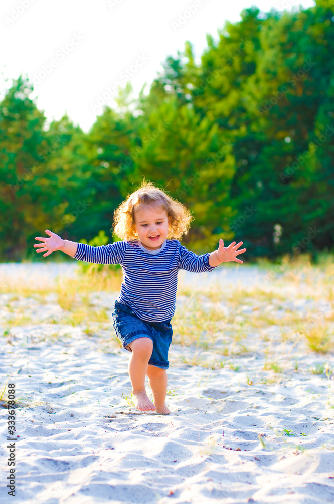 Naklejka premium vertical portrait of a little curly-haired girl running barefoot in the sand
