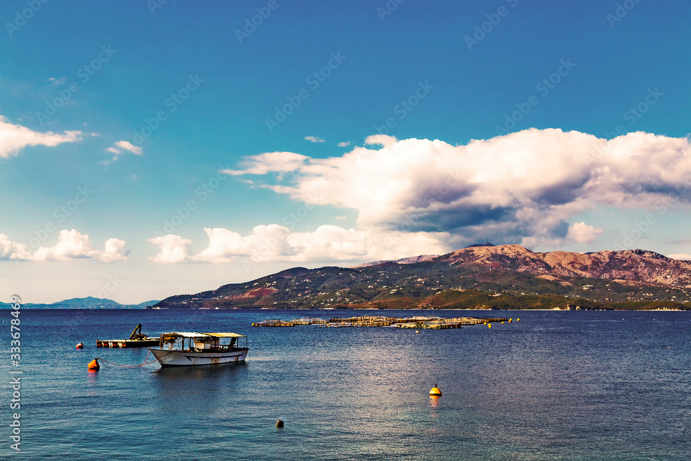 Fish farm and fisherman boat on background of Corfu island, view from Albanian coast to Corfu, Greece. Beautiful Ionian sea landscape. Sunny day, big white clouds in the sky.