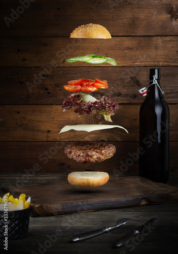 Fototapeta Naklejka Na Ścianę i Meble -  Meat burger with flying ingredients, isolated, with copyspace for text or logo, black background and bright colors