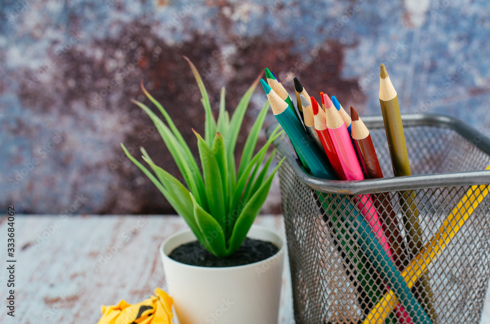 Back to school and offices stationary concept, stack of colored pens marker In a metal case, crumple paper and artificial plant on wooden desk