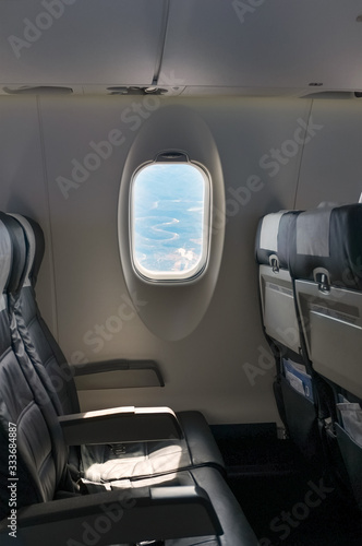 Interior of airplane flying with no passengers. View of an empty row of seats and window. Airplane is banking so you can see the a valley below from the window.