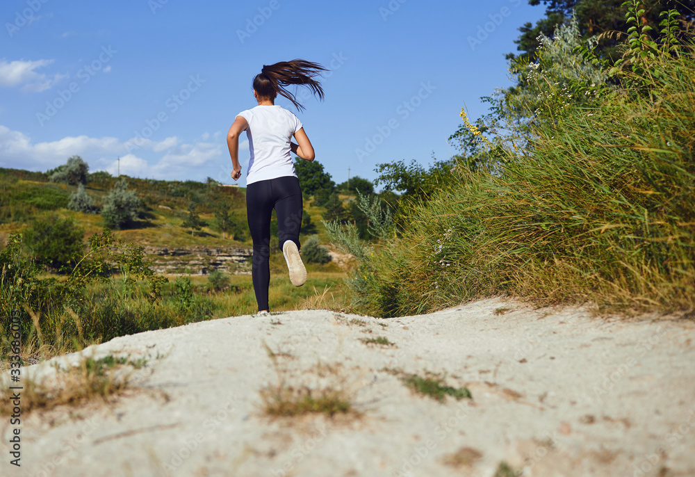 Obraz premium Girl runner runs along in nature in summer.