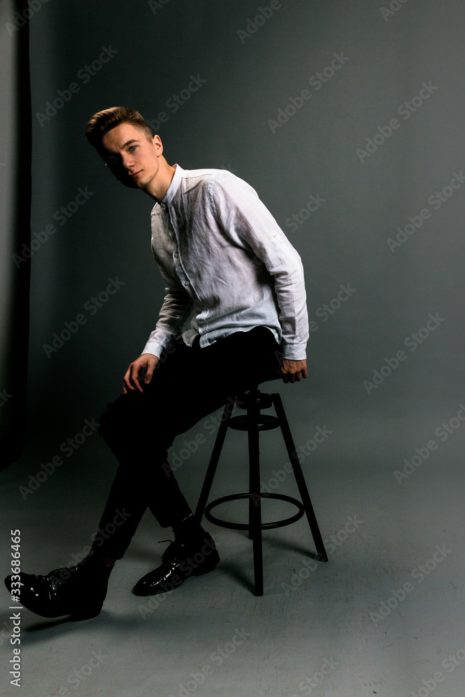 young man sitting on a chair in grey studio in white t-shirt young man sitting on a chair in grey studio in white t-shirt