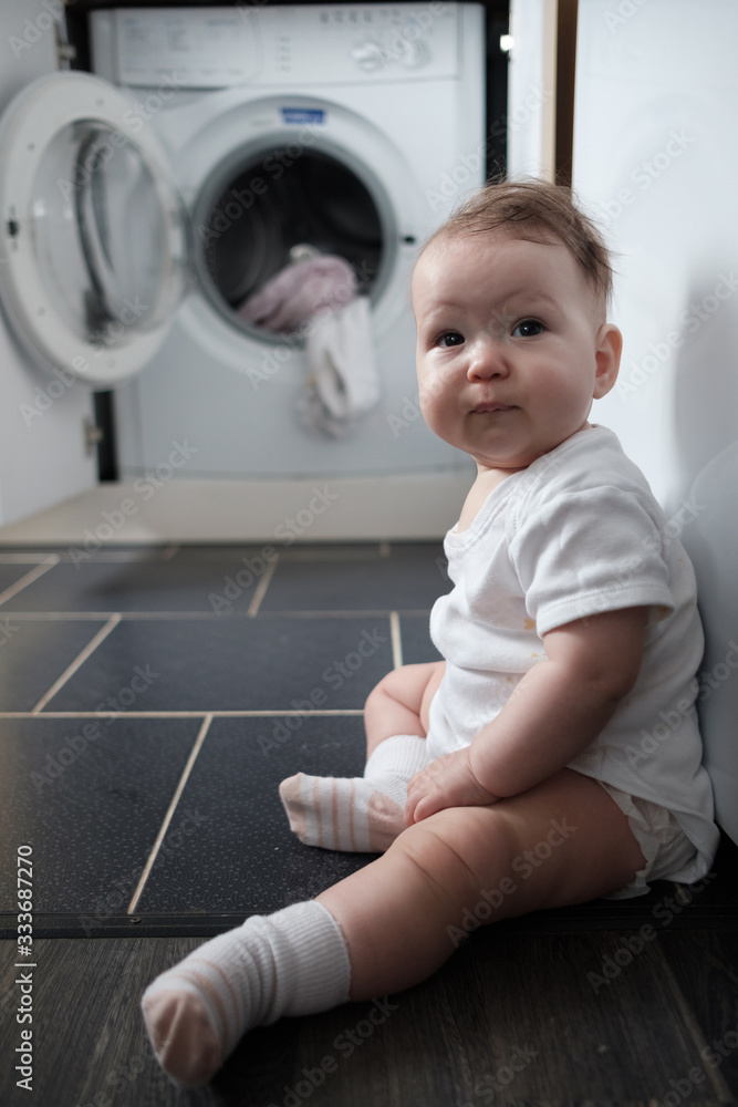 Baby girl by the washing machine in the kitchen. Baby girl by the washing machine in the kitchen.