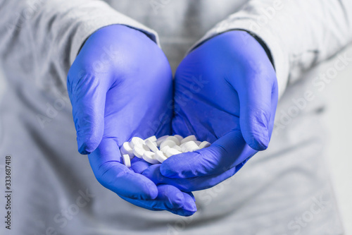 Two hands in protective medical gloves hold a handful of white pills.