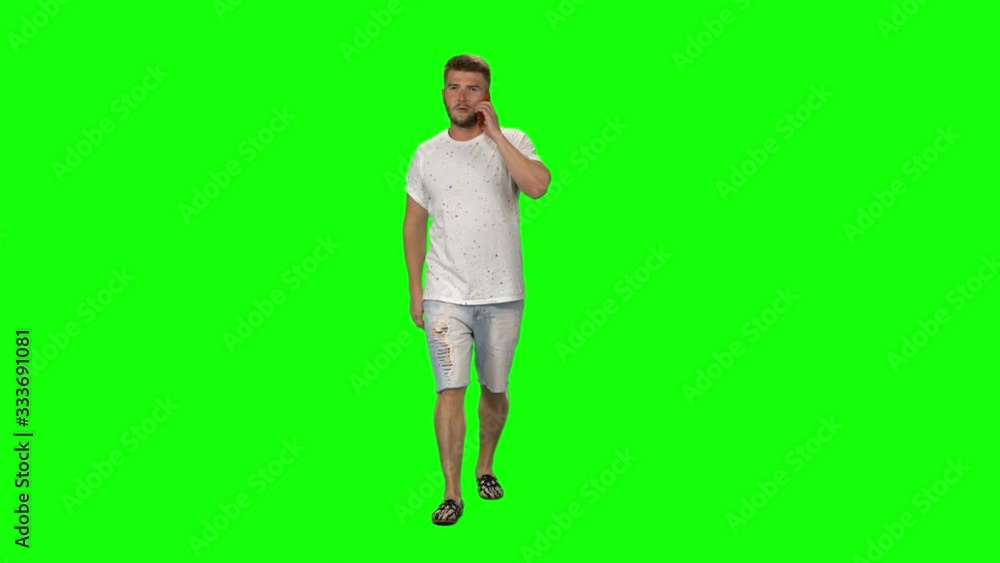 Bearded guy calmly walking and talking on the mobile phone on green screen background. Chroma key, 4k shot. Front view Bearded guy calmly walking and talking on the mobile phone on green screen background. Chroma key, 4k shot. Front view