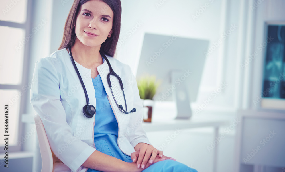 Beautiful female doctor sitting in a consulting room, smiling at the camera Beautiful female doctor sitting in a consulting room, smiling at the camera
