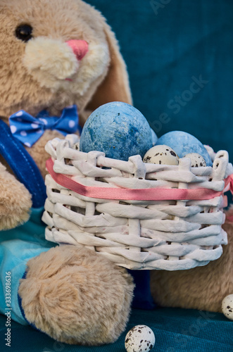 easter toy bunny holds easter basket with blue painted eggs and little queil eggs