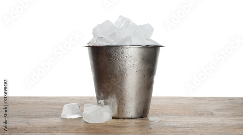 Metal bucket with ice cubes on wooden table against white background