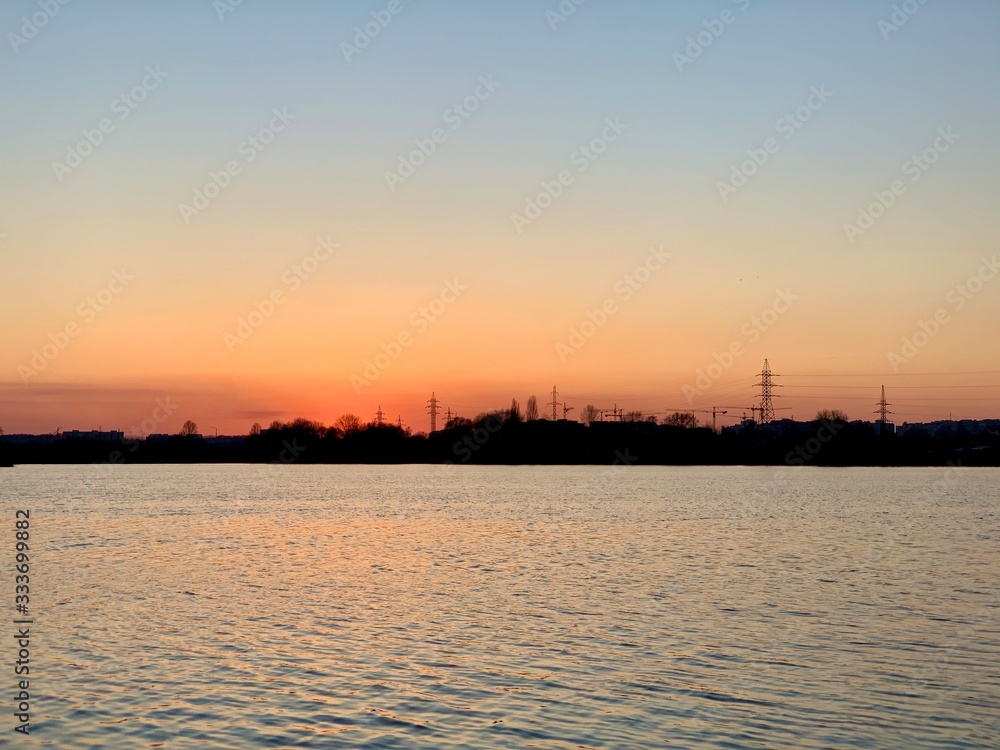 At sunset, a beautiful sky is displayed in the river. On the horizon, the shore is forcing. The sun sets over the horizon of the reservoir.