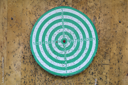 Green and white dartboard on a wooden wall photographed in Finnish summer cottage. Playing darts is a fun way to spend summer holiday. Relaxing leisure activity is also considered a sport. Closeup.