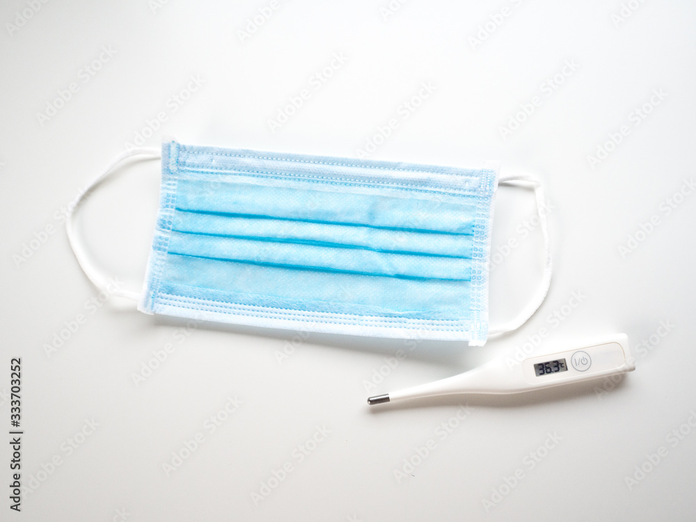 Blue surgical mask and digital thermometer on white background. Blue surgical mask and digital thermometer on white background.