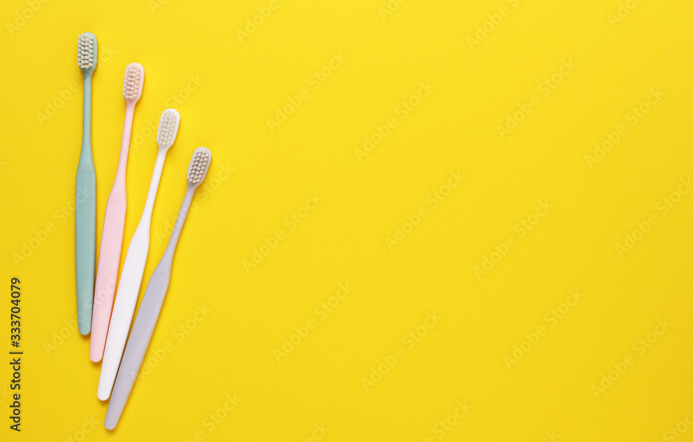 Pink, green, white and gray toothbrushes on yellow background. Taking care of teeth, dental concept. Flat lay photo, copy space, top view.