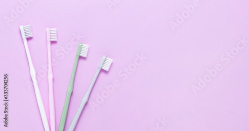 Pink, green, white and gray toothbrushes on purple background. Taking care of teeth, dental concept. Flat lay photo, copy space, top view.