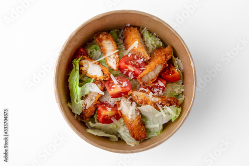 Salad of fresh herbs, lettuce, chicken fillet in a batter in a paper bowl for take away or food delivery isolated on a white background.