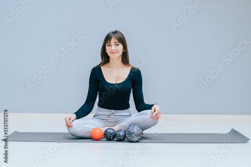 Brunette woman trainer sitting in lotus pose showing massage ball, duoball for myofascial release exircise, overcome pain, rehabilitation concept. photo