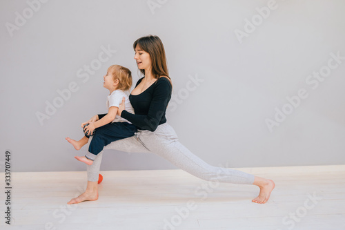 Sport, motherhood and active lifestyle concept - side view of young mother doing yoga with toddler baby at home. Lounge exercise.