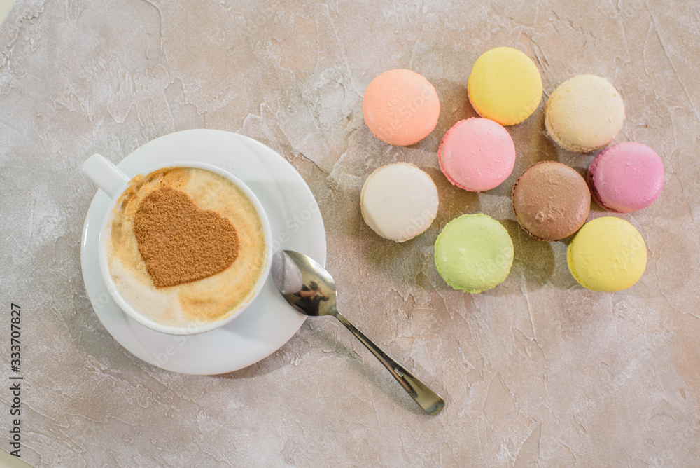 Fototapeta premium Multi-colored macarons with cappuccino on a table in a coffee shop. Sweet and tasty food