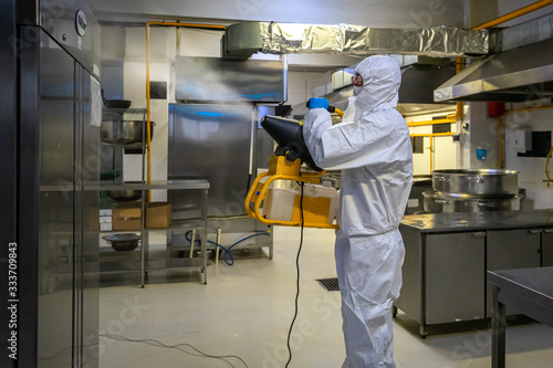 man in protective equipment disinfects with a spray gun industrial surfaces due to coronavirus covid-19 .Virus pandemic
