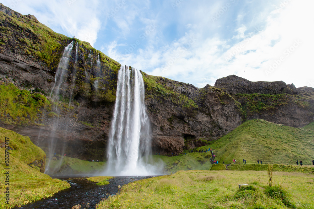 Seljalandsfoss waterfall in Iceland with blue sky and tourists Seljalandsfoss waterfall in Iceland with blue sky and tourists