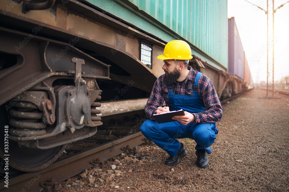 Railroad worker checking up wheels and braking system of freight train. Safety inspector or maintenance engineer checking rail tracks at station.